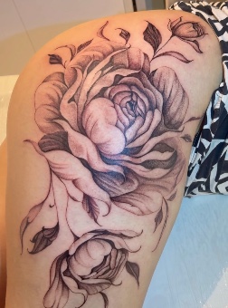 Tatuagem de flores e folhas na coxa, por Alexandre Cunha.